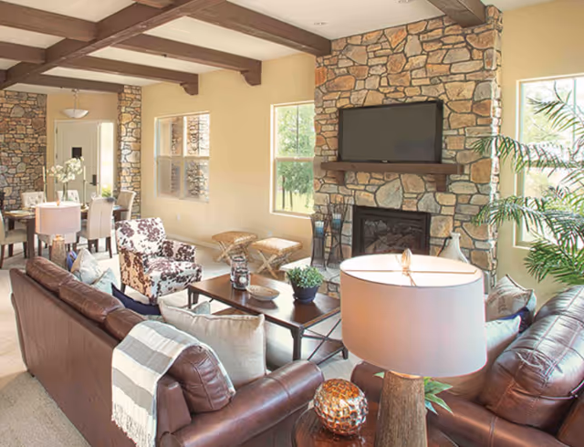 Spacious living room with brown leather sofas, a stone fireplace topped by a TV, a coffee table, and a dining area visible in the background.