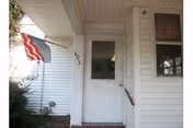 White exterior entrance with a door, small porch, and an American flag.