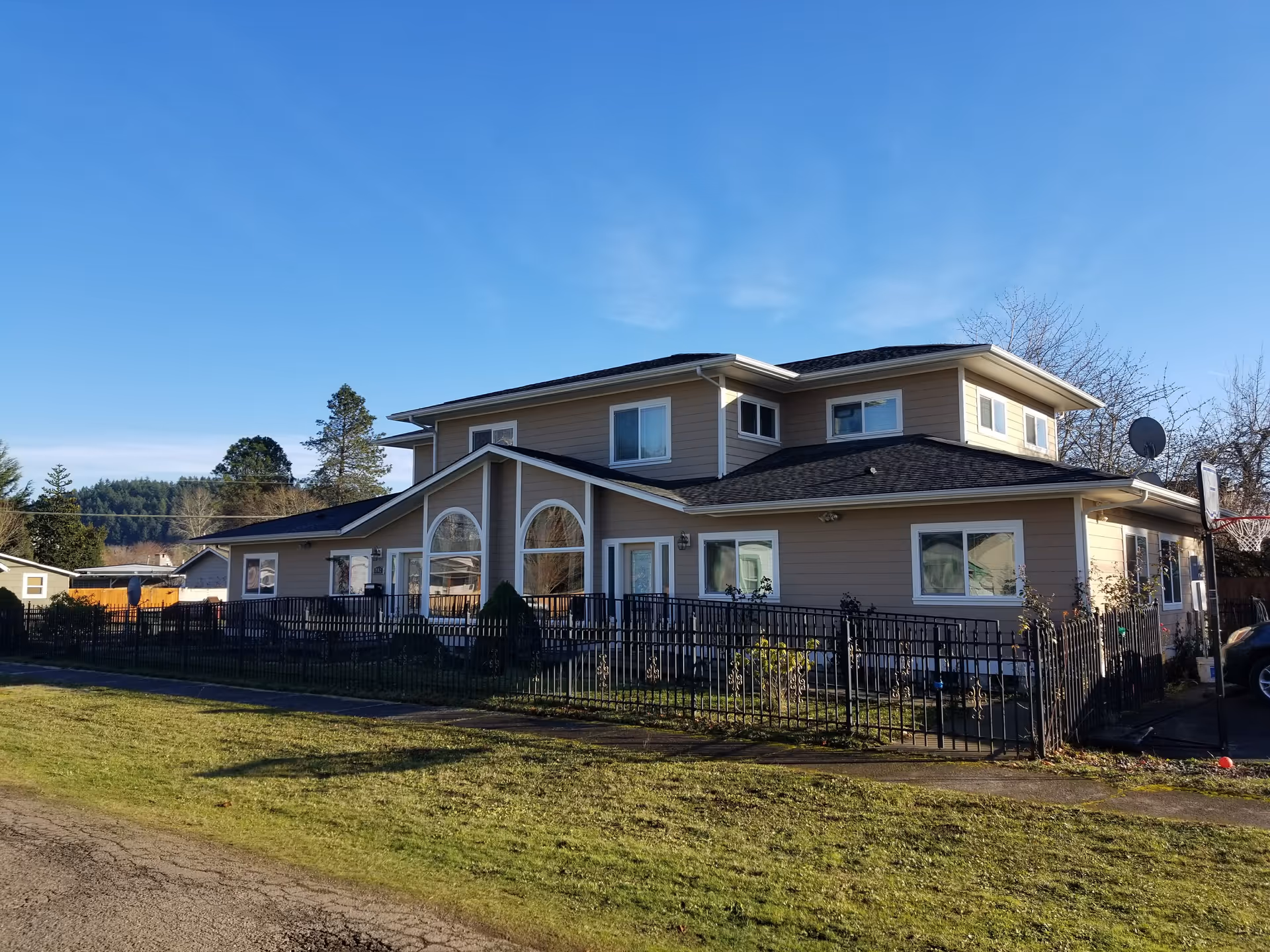 Two-story beige senior living facility with a fenced yard and curved front entrance.