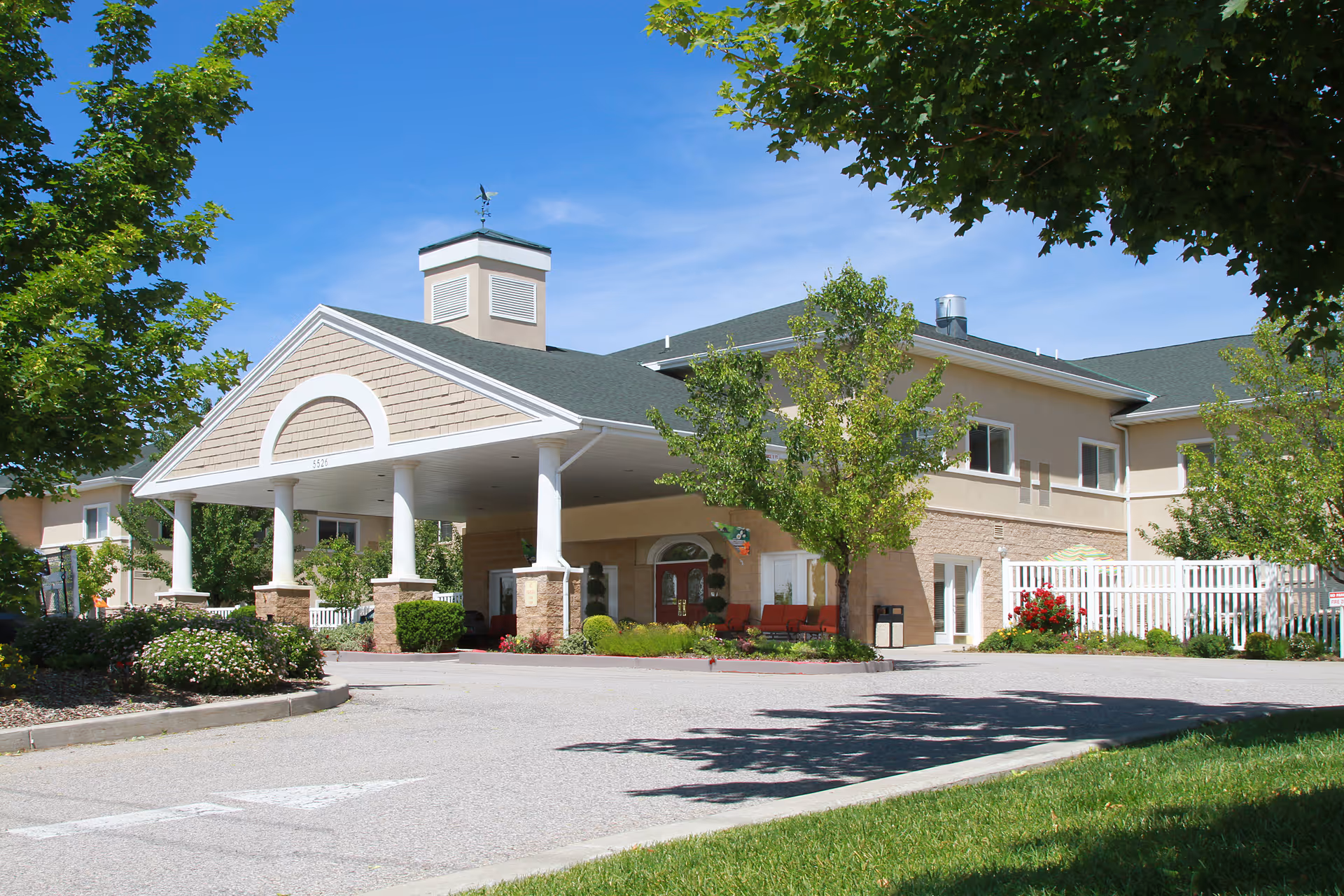 Front view of a beige assisted living facility with a covered entrance and landscaping.