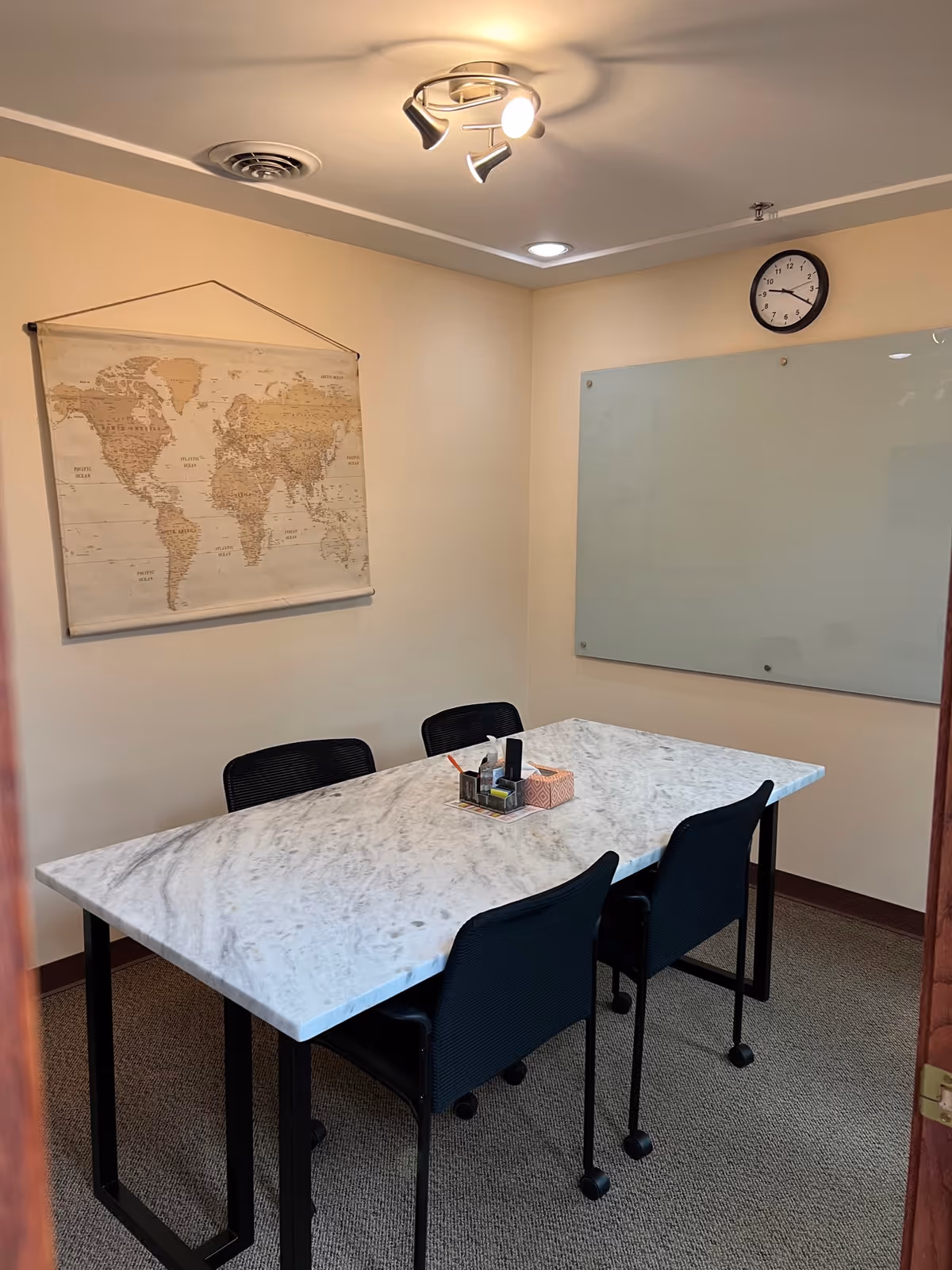 A small conference room with a marble table, world map poster, and whiteboard.