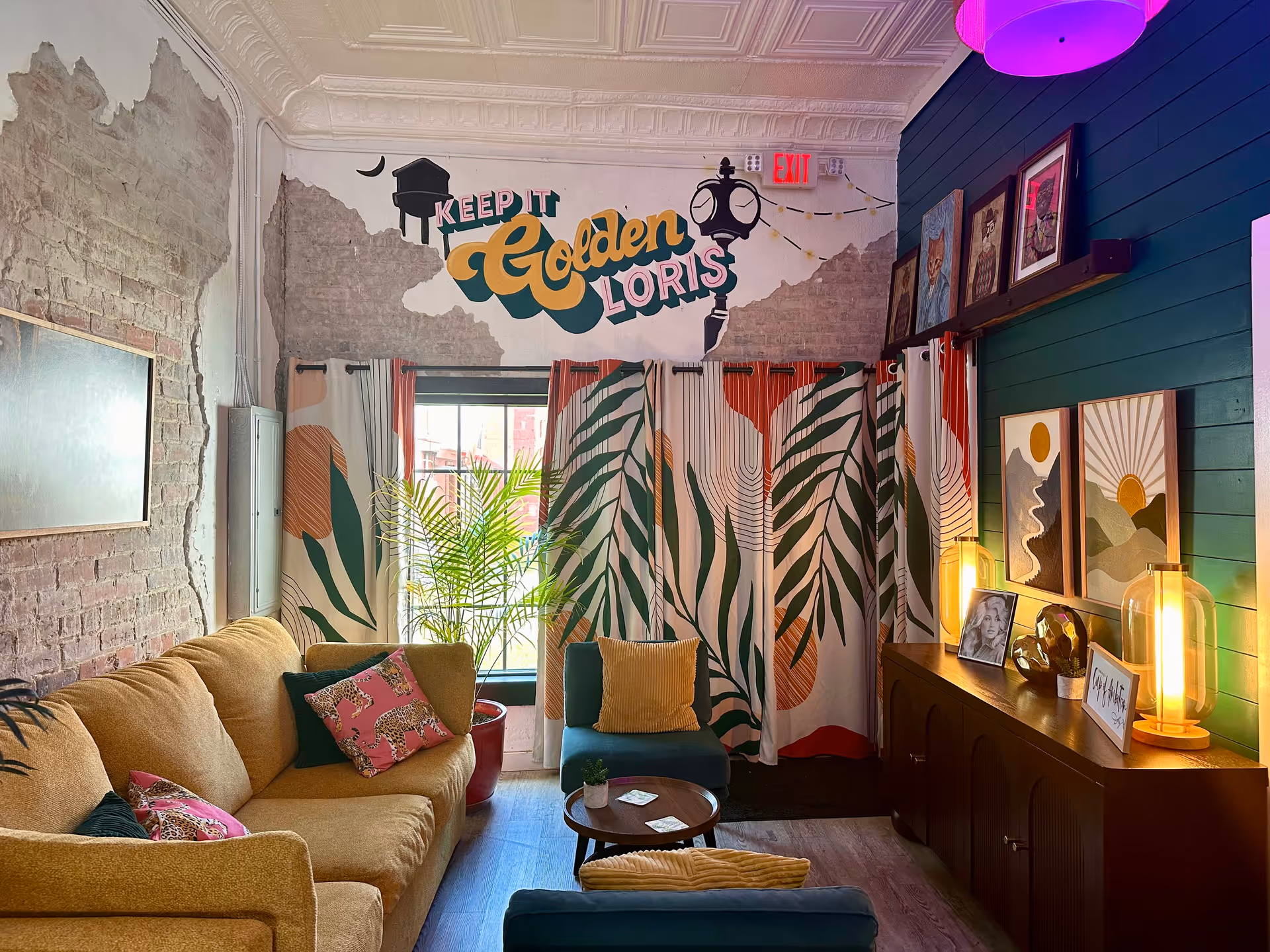 Bright living room with beige couch, tropical curtains, plant, mural, and cabinet.