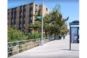 Exterior view of a brick building with trees, a walkway, and a railing along the sidewalk.
