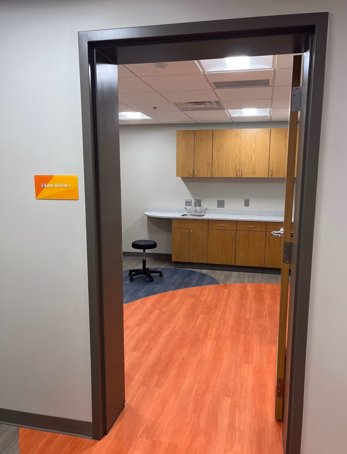 Open doorway to a room with wooden cabinets, a sink, counter, and exam room sign