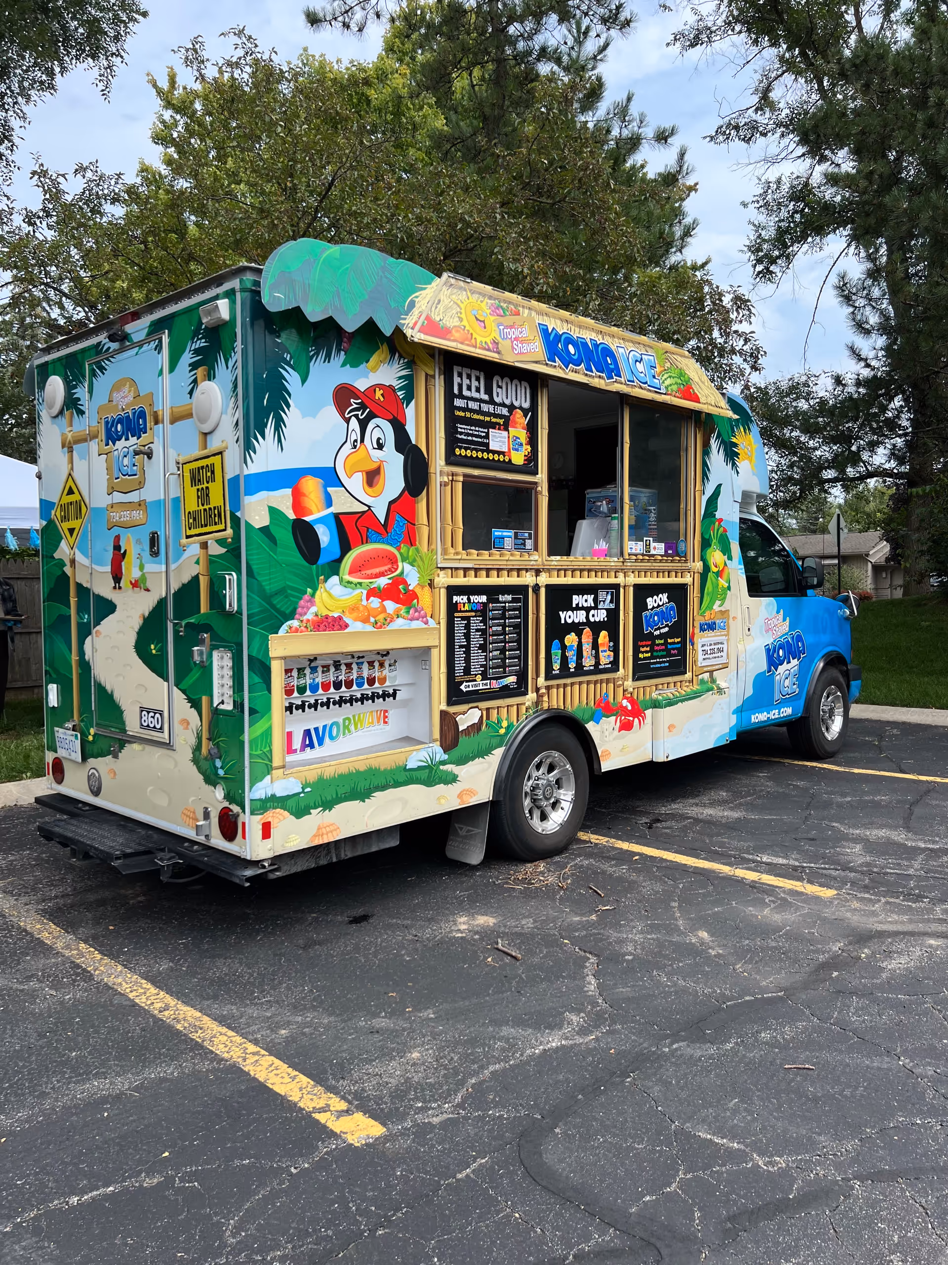 Colorful Kona Ice truck parked in a lot with tropical-themed artwork.