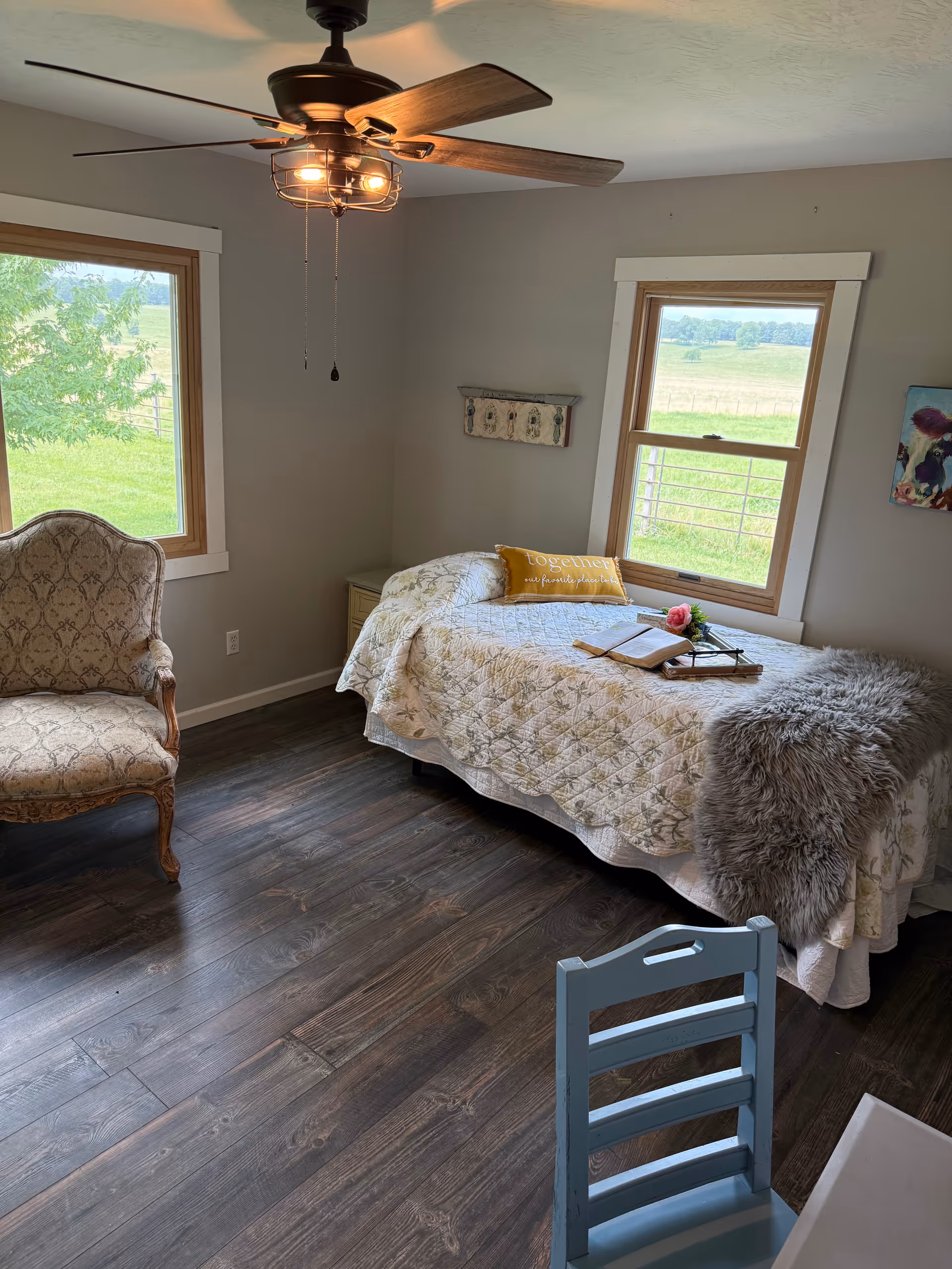 Cozy bedroom with a bed, chair, two windows, and a ceiling fan.