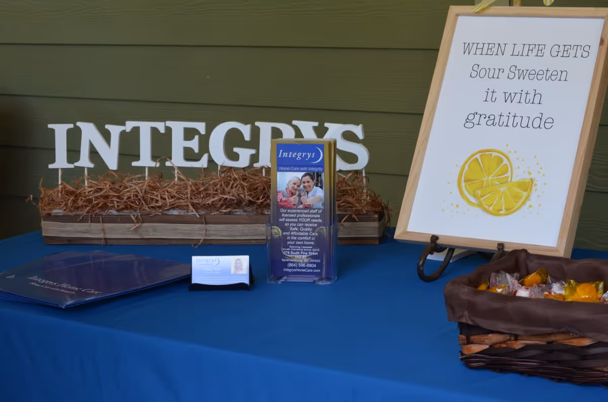 Promotional table display with Integrys Home Caregiving signage, brochures, and a lemon-themed sign.