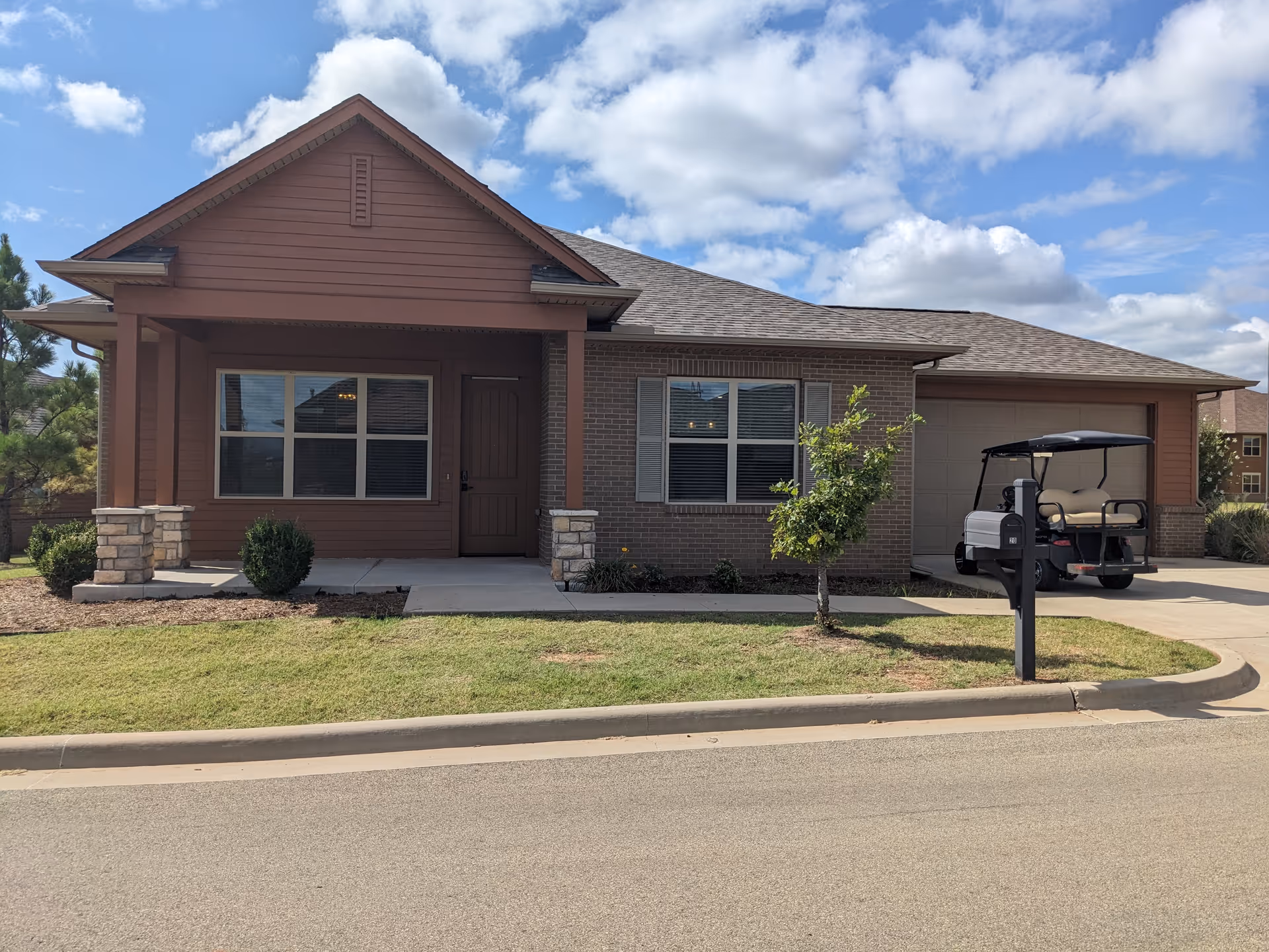 Front view of a single-story brown brick senior living building with a driveway and golf cart.
