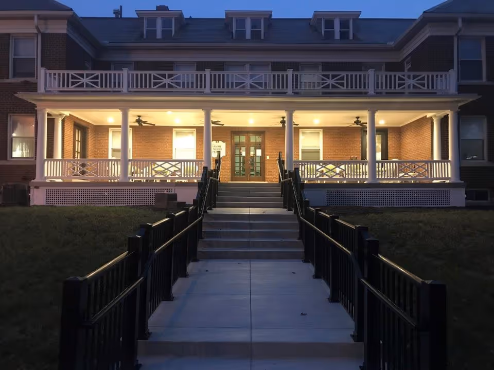 Brick senior living facility with a lit covered porch and white railings.