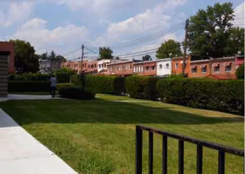 Outdoor lawn with a concrete path, trimmed hedges, and brick buildings in the background.