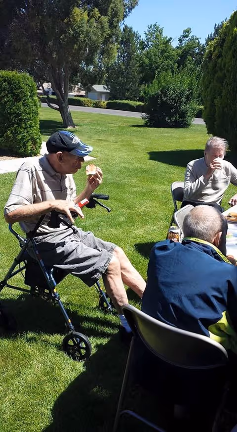 Elderly residents sit and eat at a sunny outdoor lawn gathering.