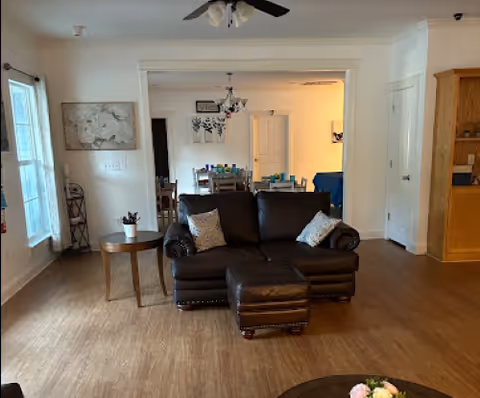 A dark brown leather sofa with cushions sits in a bright, open living room.