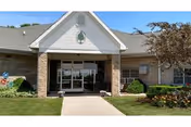 Front entrance of a single-story senior facility with glass doors and landscaping.
