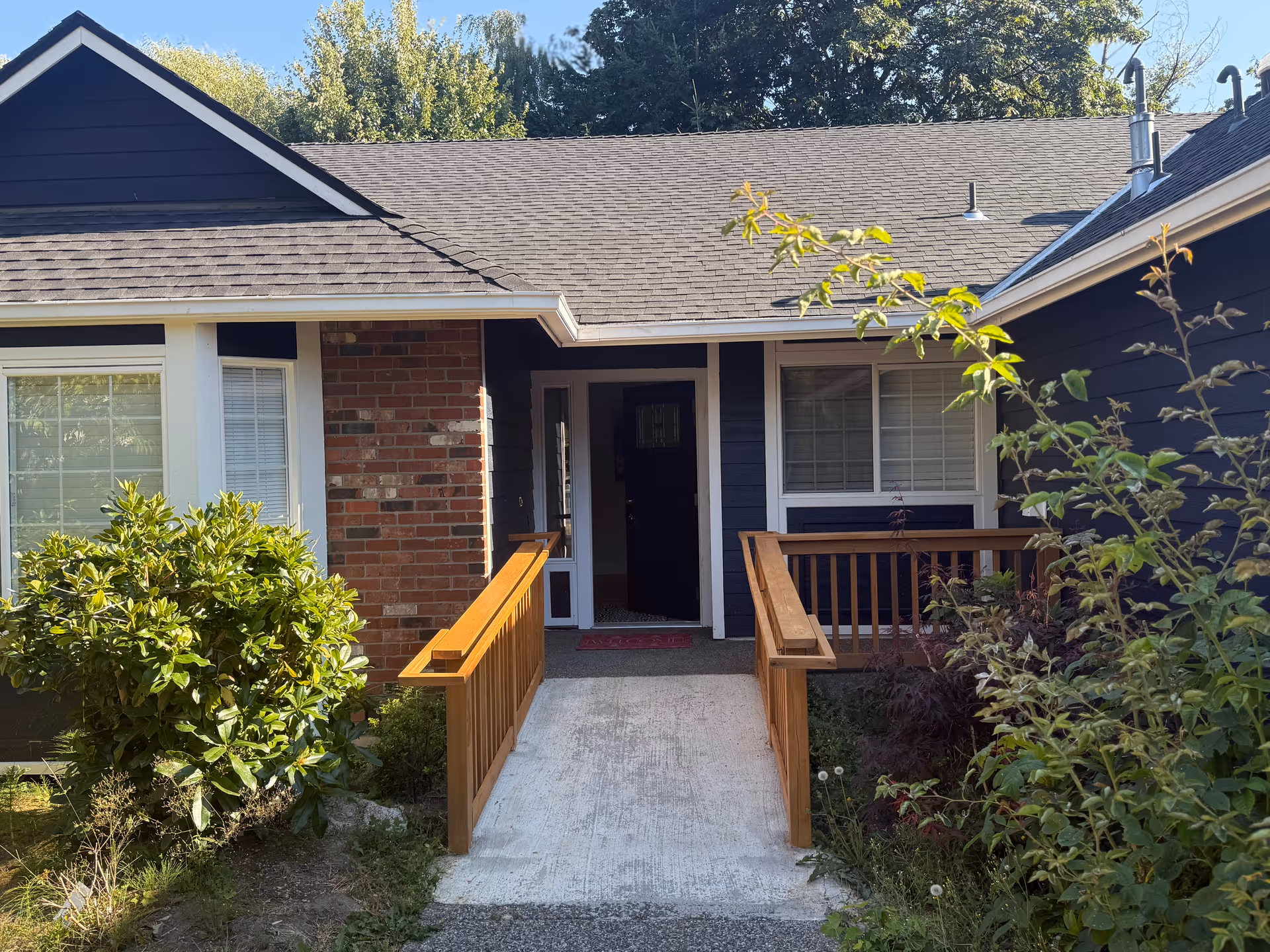 Front entrance of a blue, single-story senior living facility with a wooden ramp and garden.