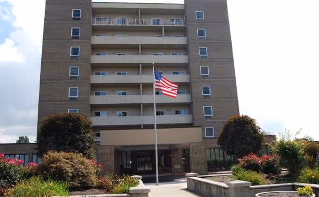 Exterior view of Oak Hill Village senior living building with flag and landscaped entrance.