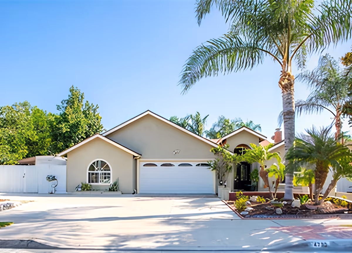 Single-story beige building with an attached garage, driveway, and palm trees in the front yard.