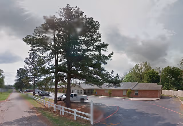 Exterior view of a single-story brick senior living facility with parking lot and tall trees.