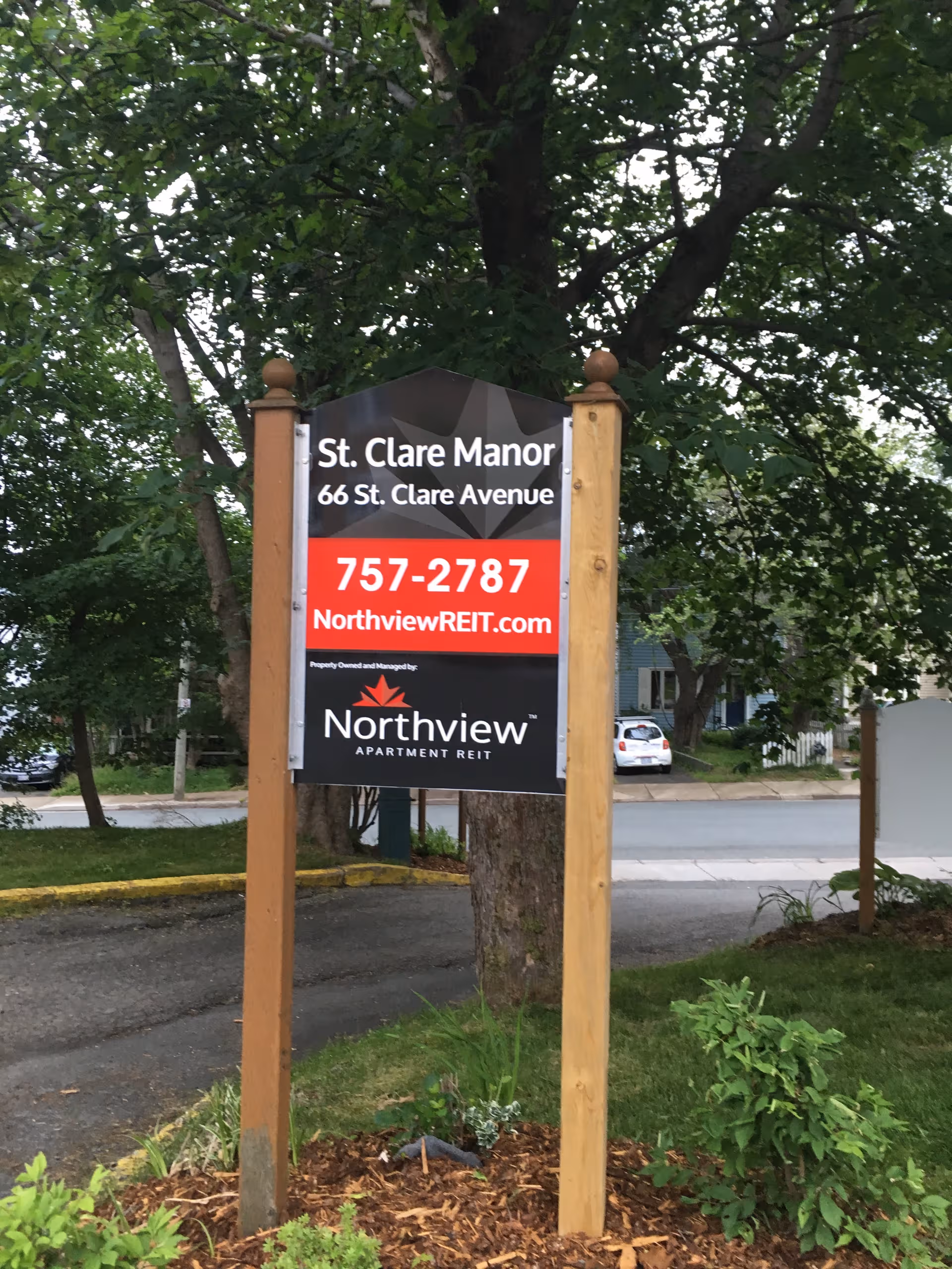 Outdoor wooden-post sign announces St. Clare Manor Nursing Home in front of trees.