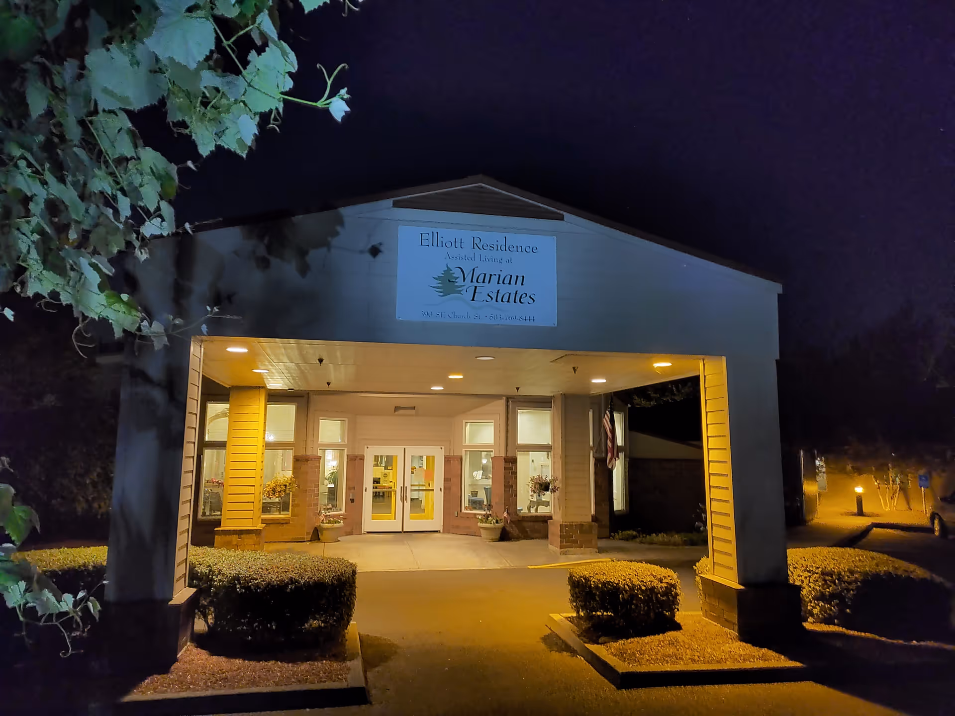 Night exterior of Elliott Residence assisted living entrance with glass doors and signage.