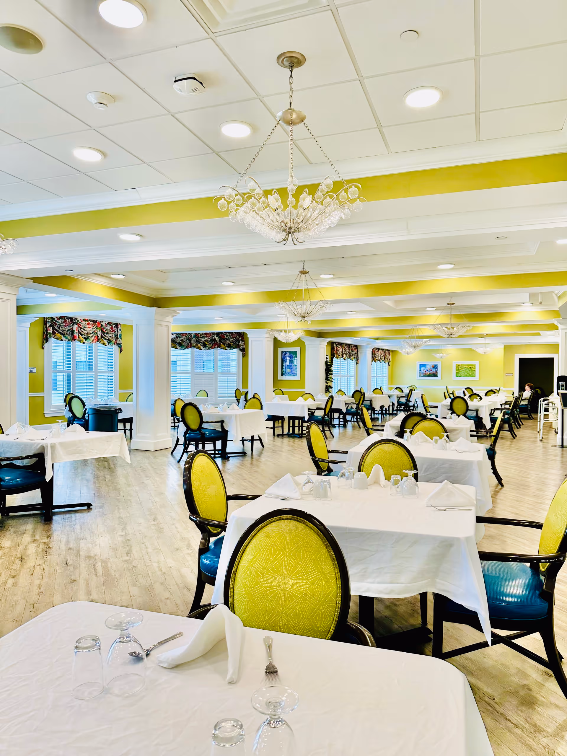 Bright dining hall with white tablecloths, lime chairs, and crystal chandeliers.