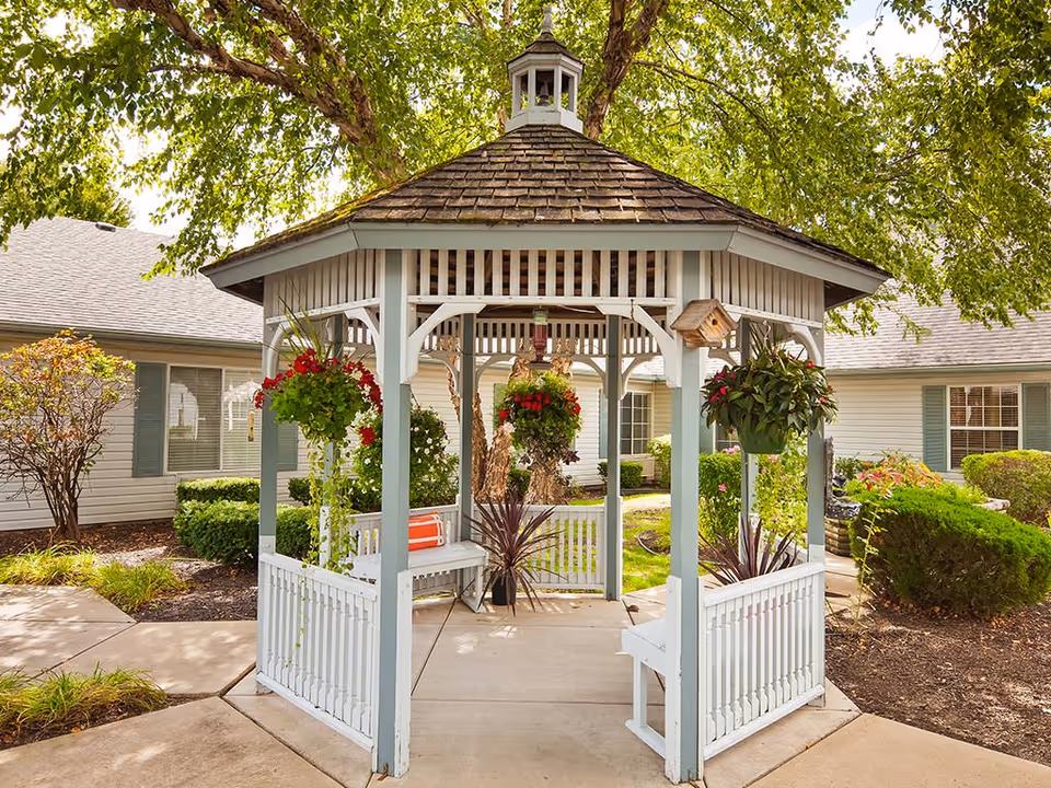 White wooden gazebo with hanging flower baskets in a landscaped courtyard outside the Windsor of Lawrence building.