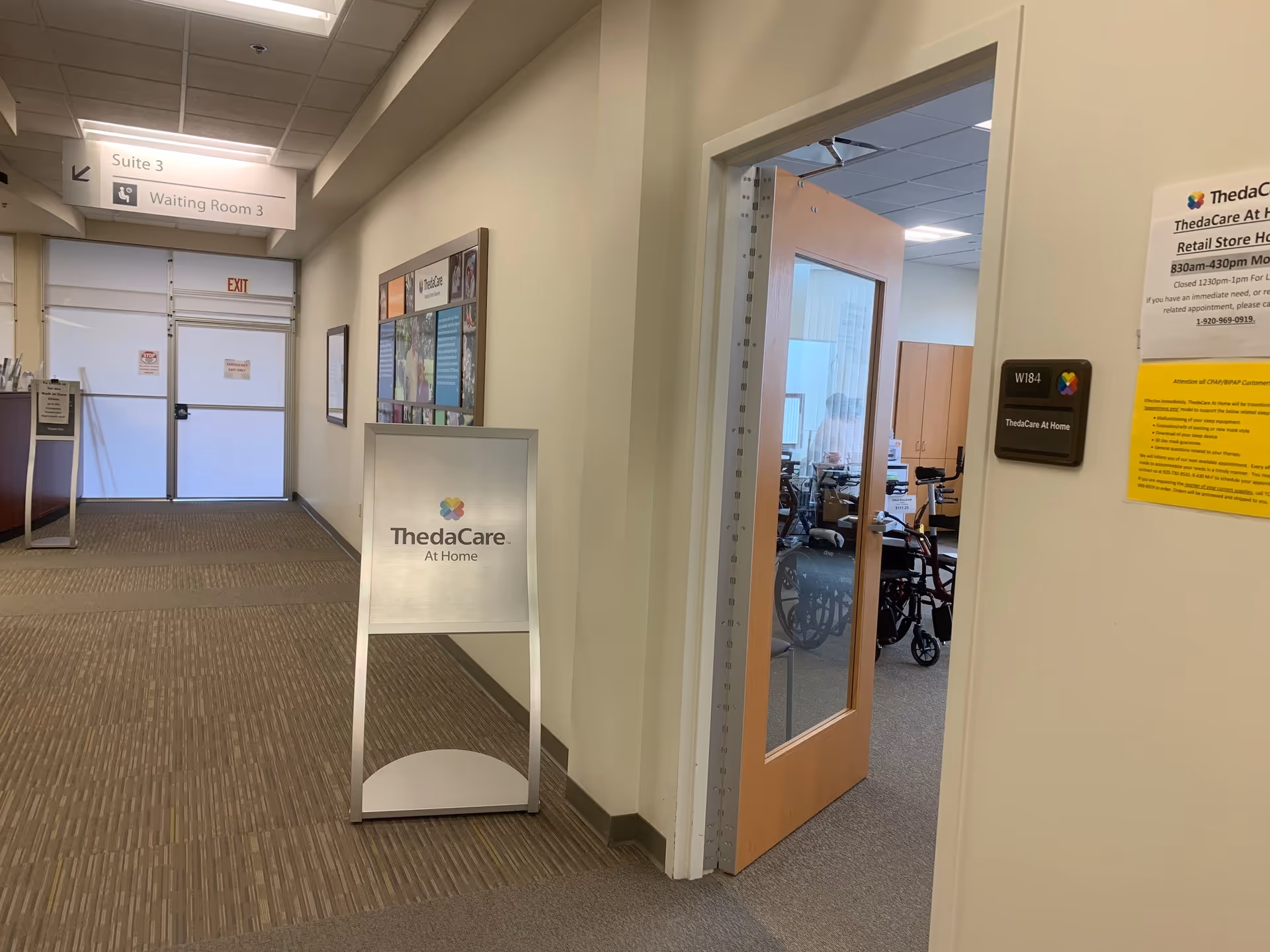 Hospital-like corridor with signage, a glass door, and a waiting area.