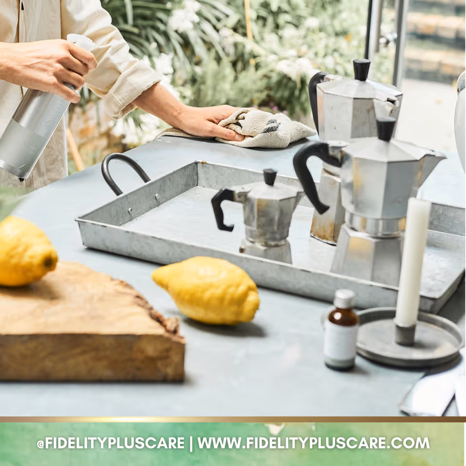 Person wipes a kitchen counter with a towel while coffee pots and lemons sit nearby.