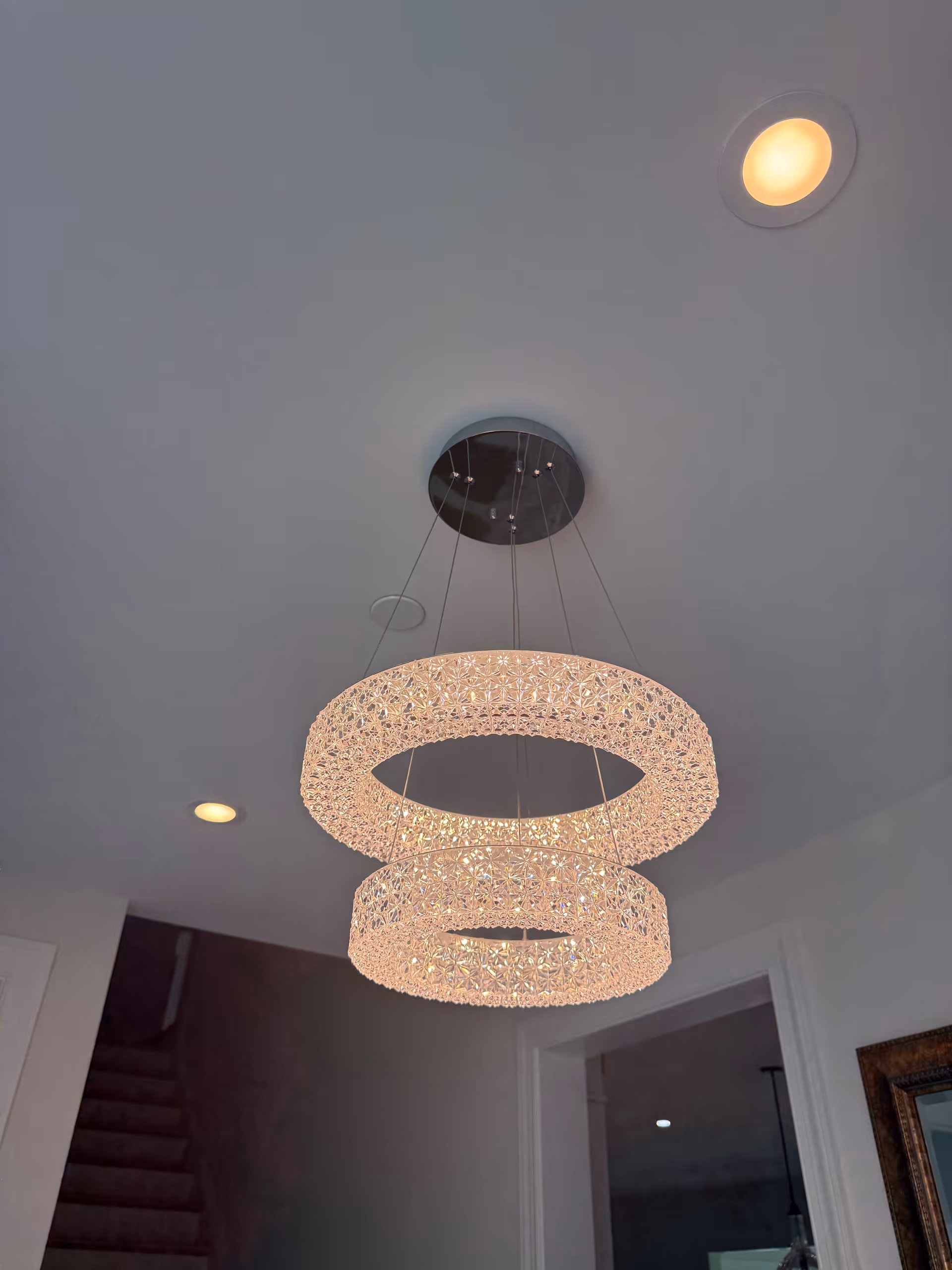 Elegant crystal chandelier suspended from a ceiling over a hallway staircase in a senior living facility.