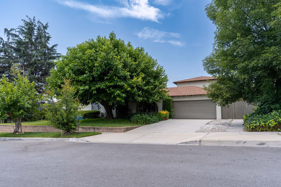 Residential front exterior with driveway, garage, and lush trees surrounding a single-story house.