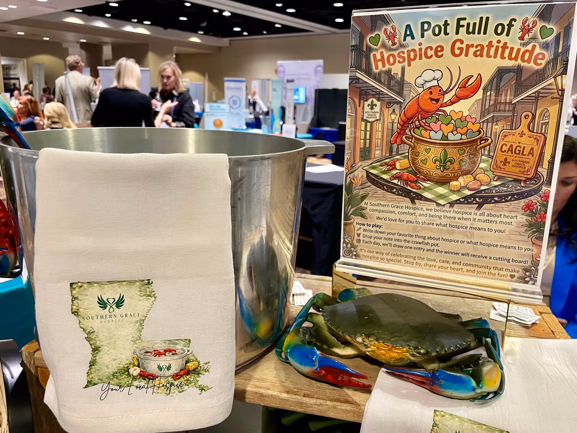 Indoor hospice expo booth with a metal bucket, Southern Grace cloth, and a colorful gratitude poster.