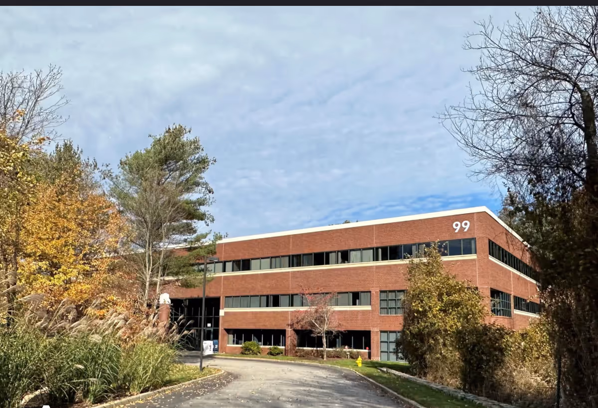 Three-story red brick building exterior with large windows and surrounding autumn trees.