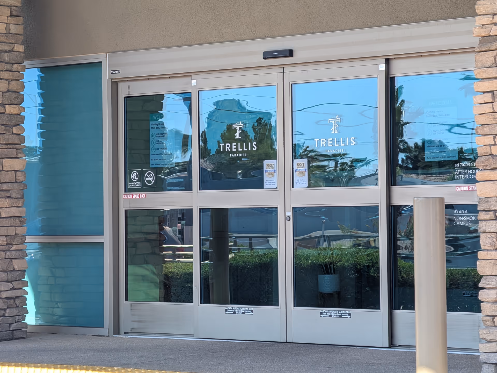 Glass double doors with Trellis Paradise logos, stone walls, and tan exterior facade.