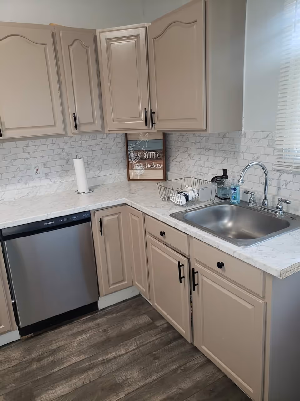 L-shaped kitchen with beige cabinets, marble countertops, sink, and dishwasher
