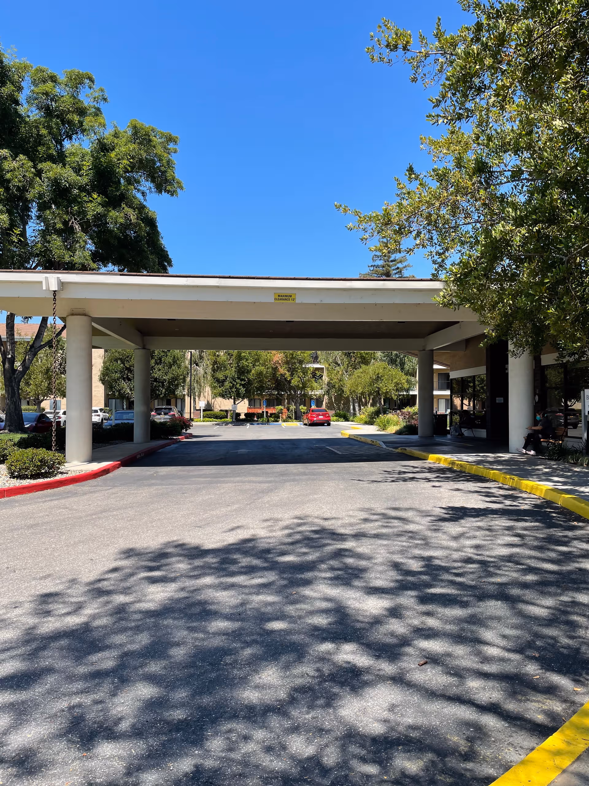 Covered drive-through entrance at Brookdale San Jose, with cars, trees, and a bright blue sky.