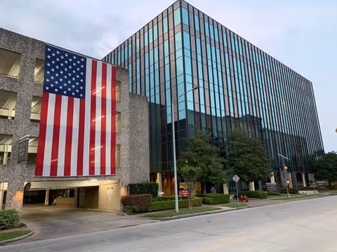 A modern multi-story building facade with a large American flag displayed beside the entrance.