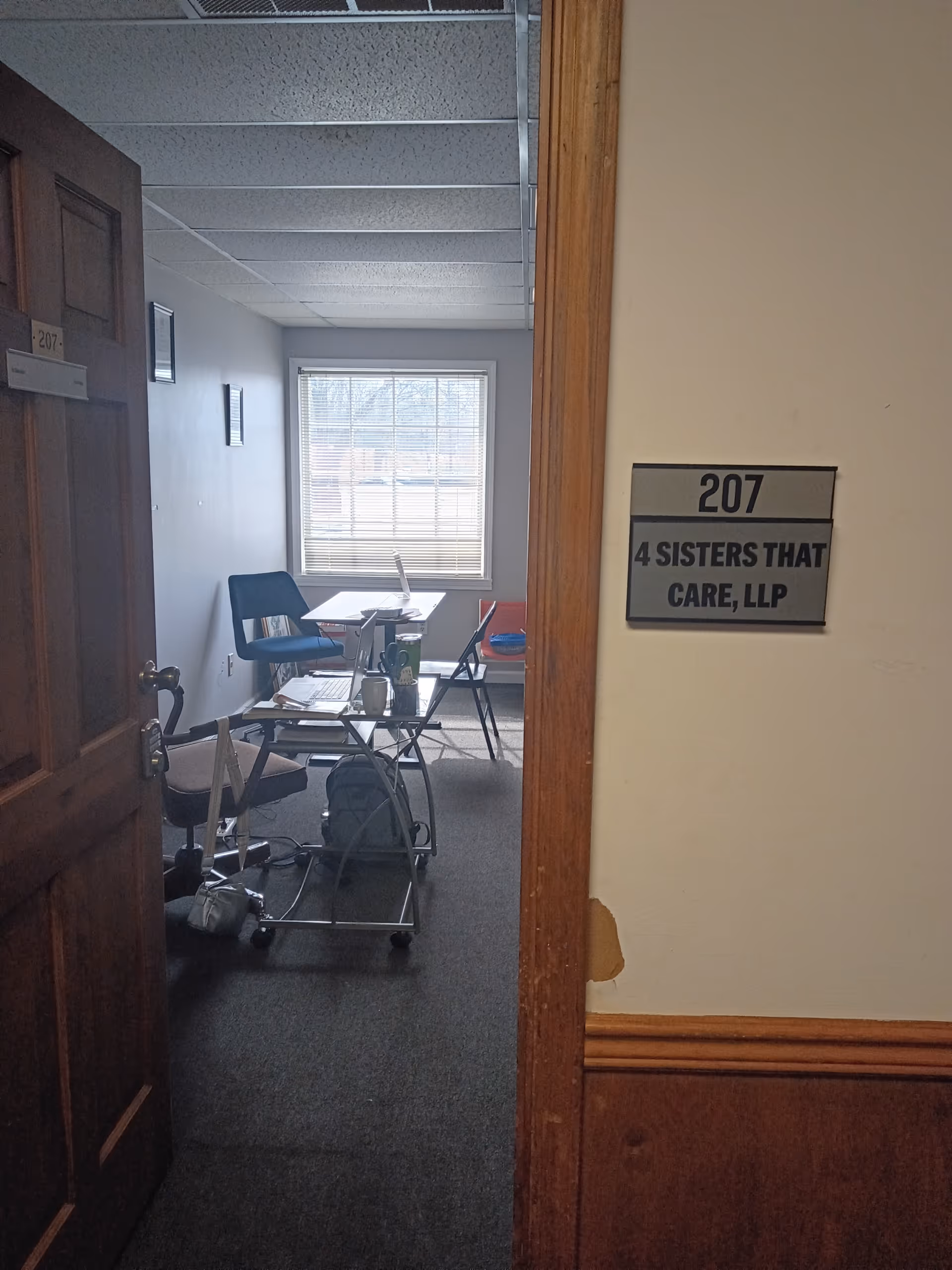 Office-style room with desk, chairs, computer, and a window; sign reads 4 Sisters That Care.