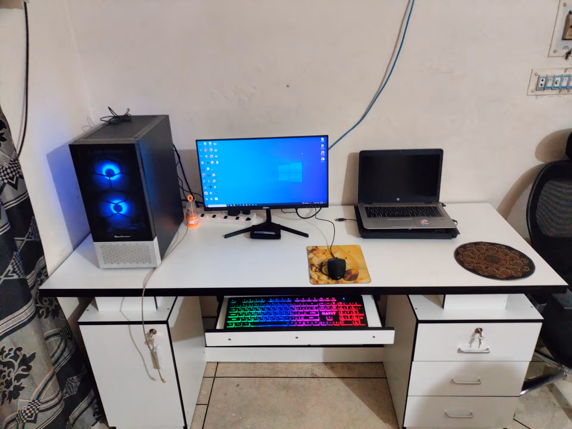 Desk setup with monitor, laptop, rainbow RGB keyboard, and mouse in a tidy interior room.