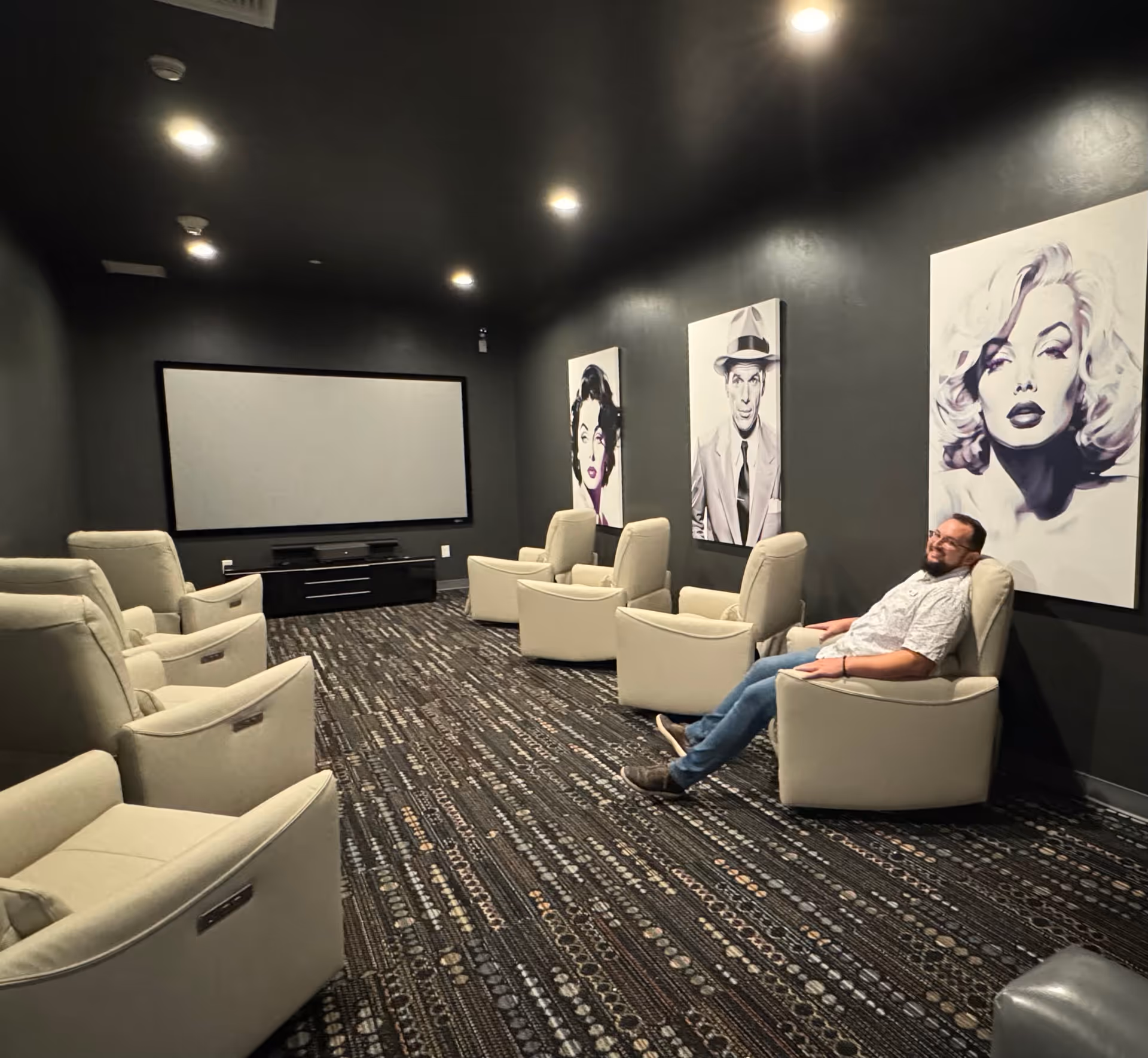 Dimly lit lounge with beige recliners facing a large screen.
