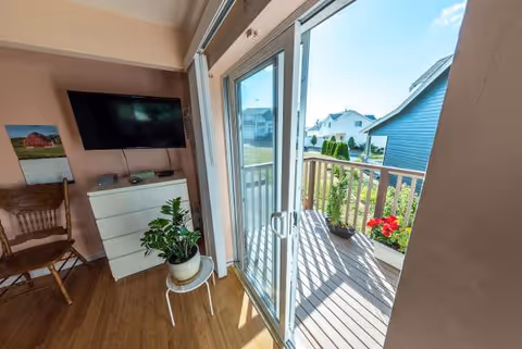 Cozy living area with a TV, dresser, plant, and balcony access through glass doors.