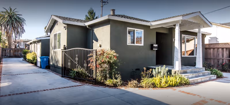 Exterior view of a single-story gray building with a front porch and gate.