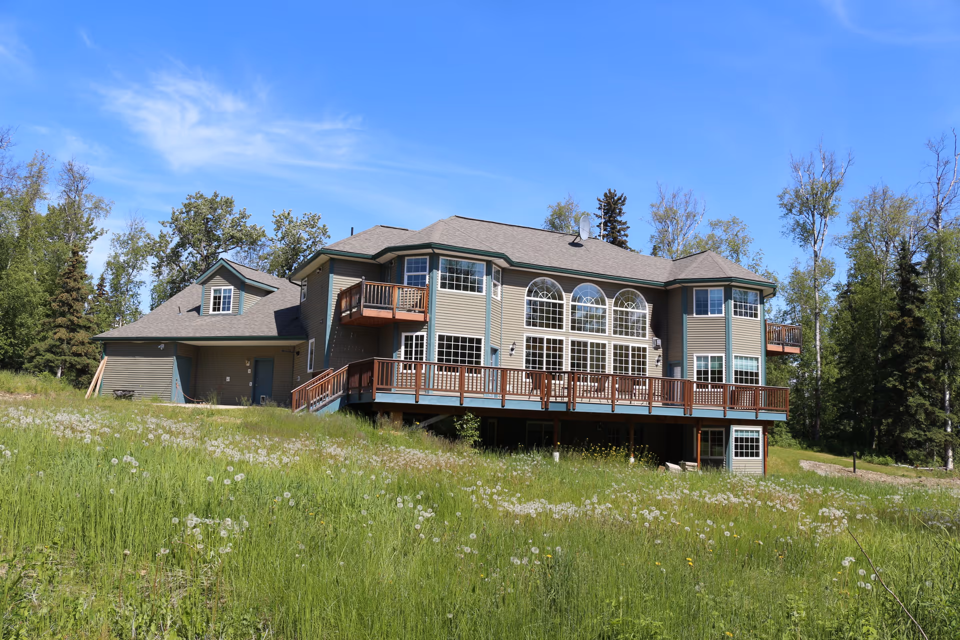 A multi-story house-style senior living facility on a grassy field beneath a blue sky.