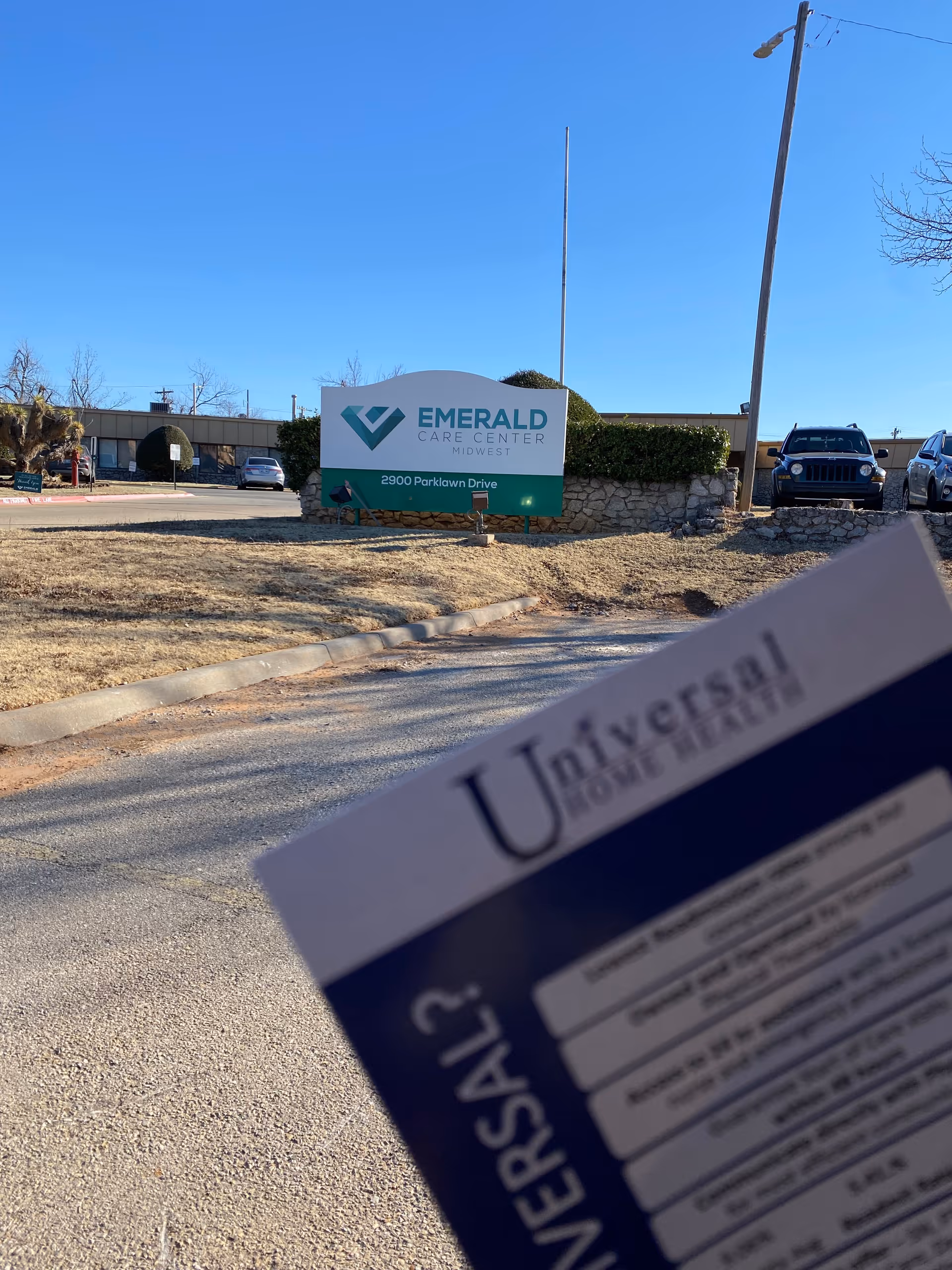 Outside view of Emerald Care Center sign with parking lot and foreground Universal Home Health card.