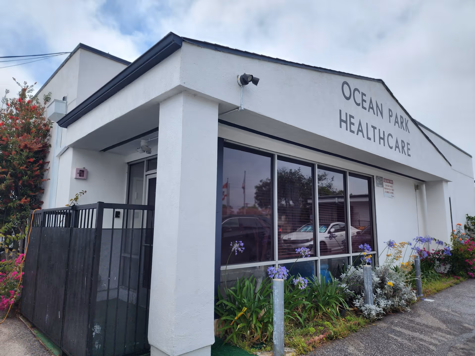 White exterior healthcare building with large windows and colorful flowers along the entrance.