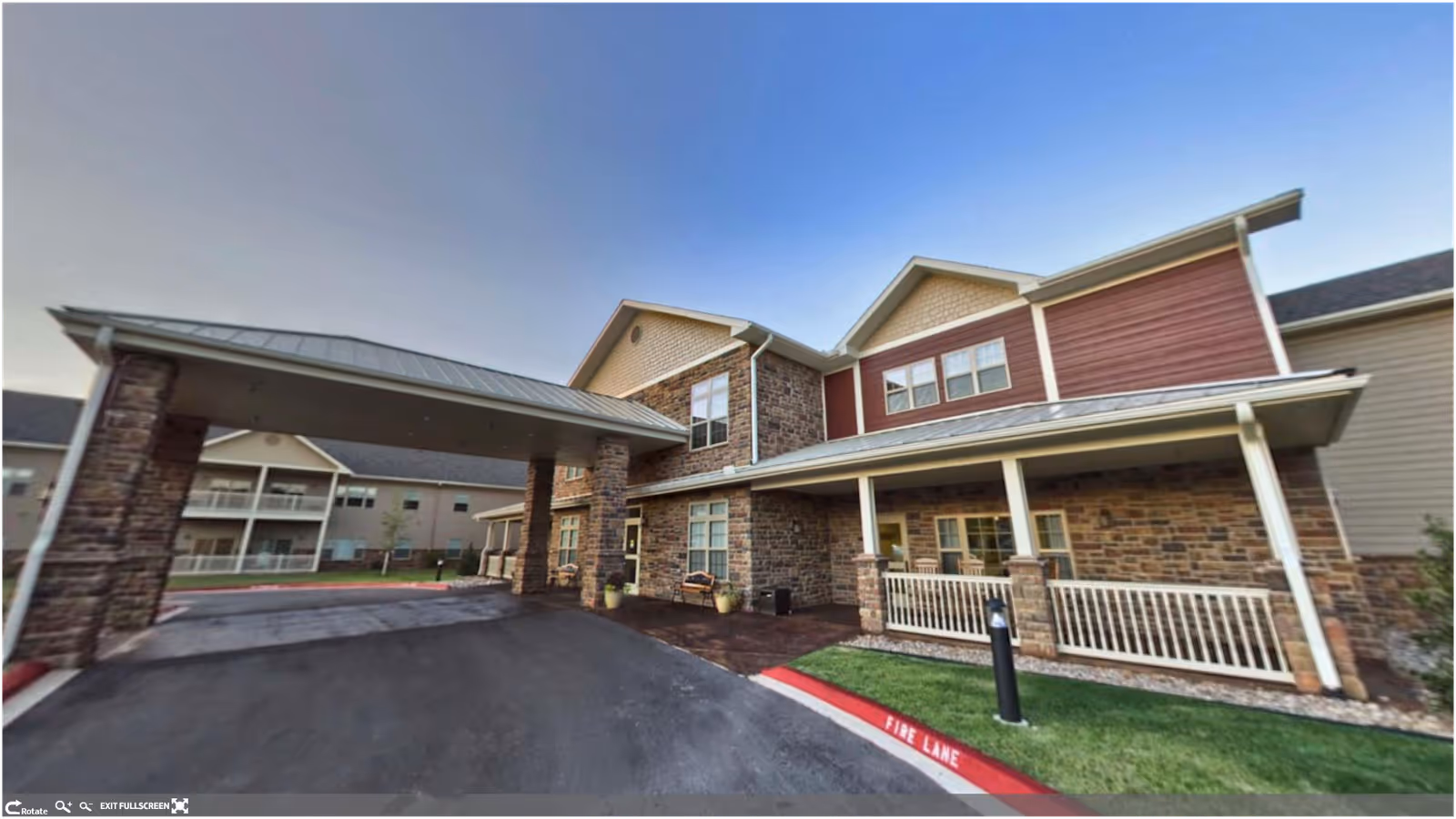 Front entrance of a two-story senior living building with a covered porte-cochere and stone-and-siding facade.