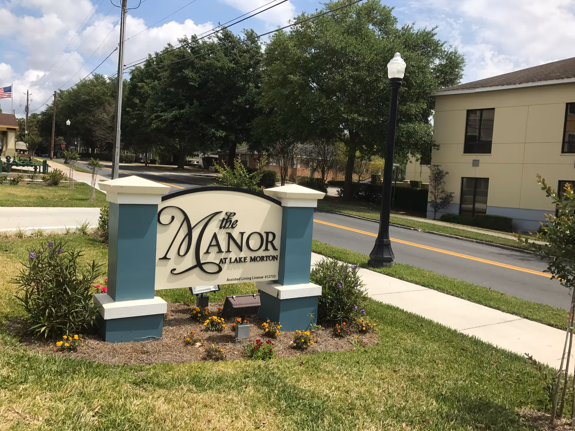 Entrance sign reading 'The Manor at Lake Morton' on a landscaped lawn with a road and buildings in the background.