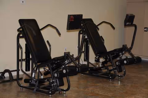 Two black exercise machines sit in a small indoor gym with beige walls.