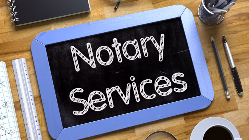 Blue-framed chalkboard on a desk displays Notary Services beside pencils and a coffee cup.