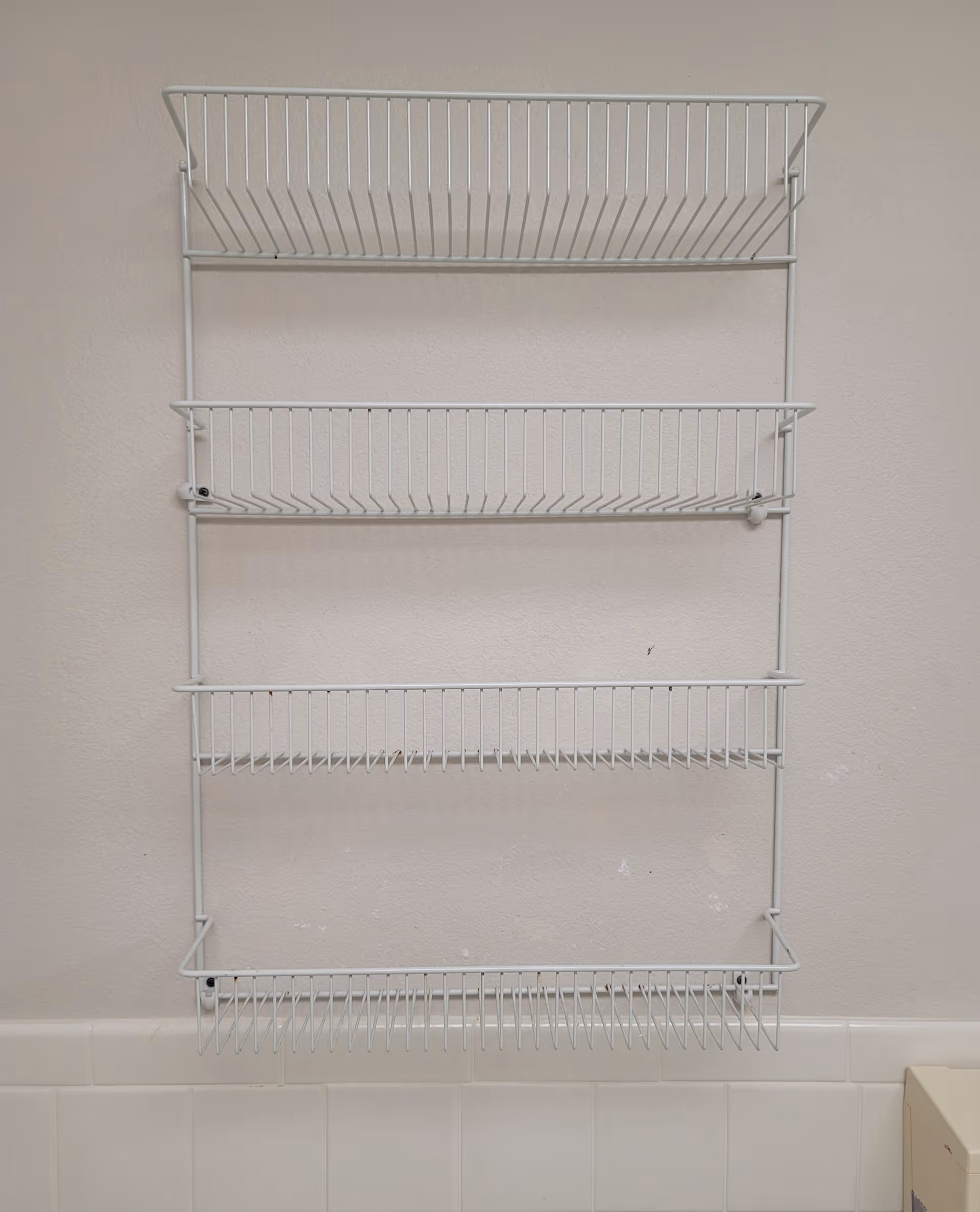Tall white metal wire shelving unit mounted on a beige wall with tiled base.