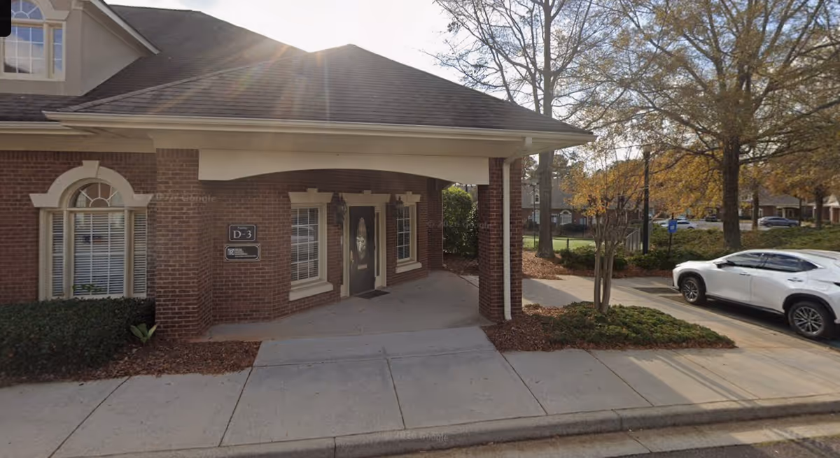Brick senior living facility exterior with covered entrance and parked white car.