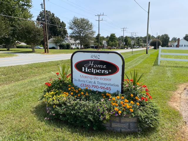 Sign for Home Helpers Home Care surrounded by colorful flowers on a grassy roadside.